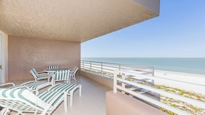 A balcony with white railings, a table, and striped lounge chairs overlooking a beach. - Experience coastal comfort at The Somerset, your oceanfront haven on Marco Island (Marco Island)
