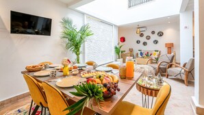 Ein Essbereich mit einem für das Frühstück gedecktem Tisch, einem an der Wand befestigten Fernseher und einem Balkon mit Geländer.