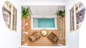 Ein Poolbereich mit Fliesenboden, zwei Sitzbereichen mit Kissen und einer Wand mit einem gemusterten Teppich.