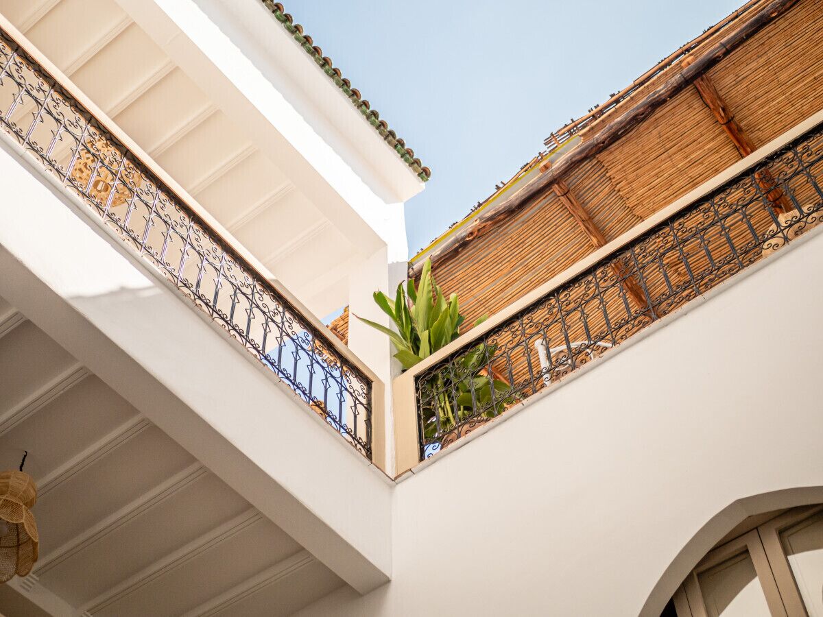 A corner of a building with white walls, a balcony with metal railings, and a plant on the balcony.