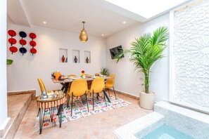 A dining area with a table set for four, surrounded by yellow chairs, a patterned rug, and a hanging pendant light. - Riad Mélina-Au Coeur de la Médina - Breakfast (Marrakech)