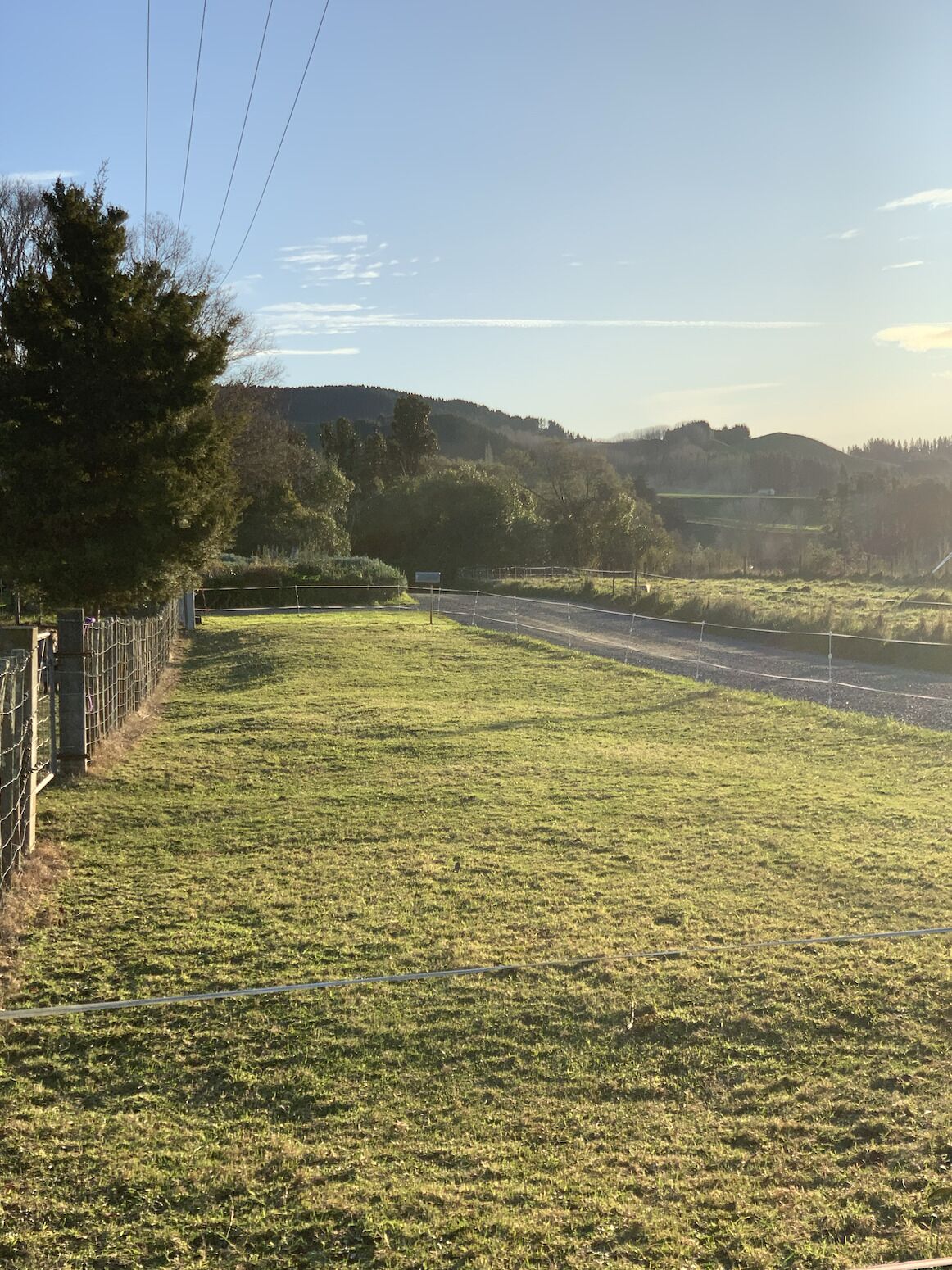 Ein grasbewachsenes Feld mit einem Zaun und einer Straße im Hintergrund.