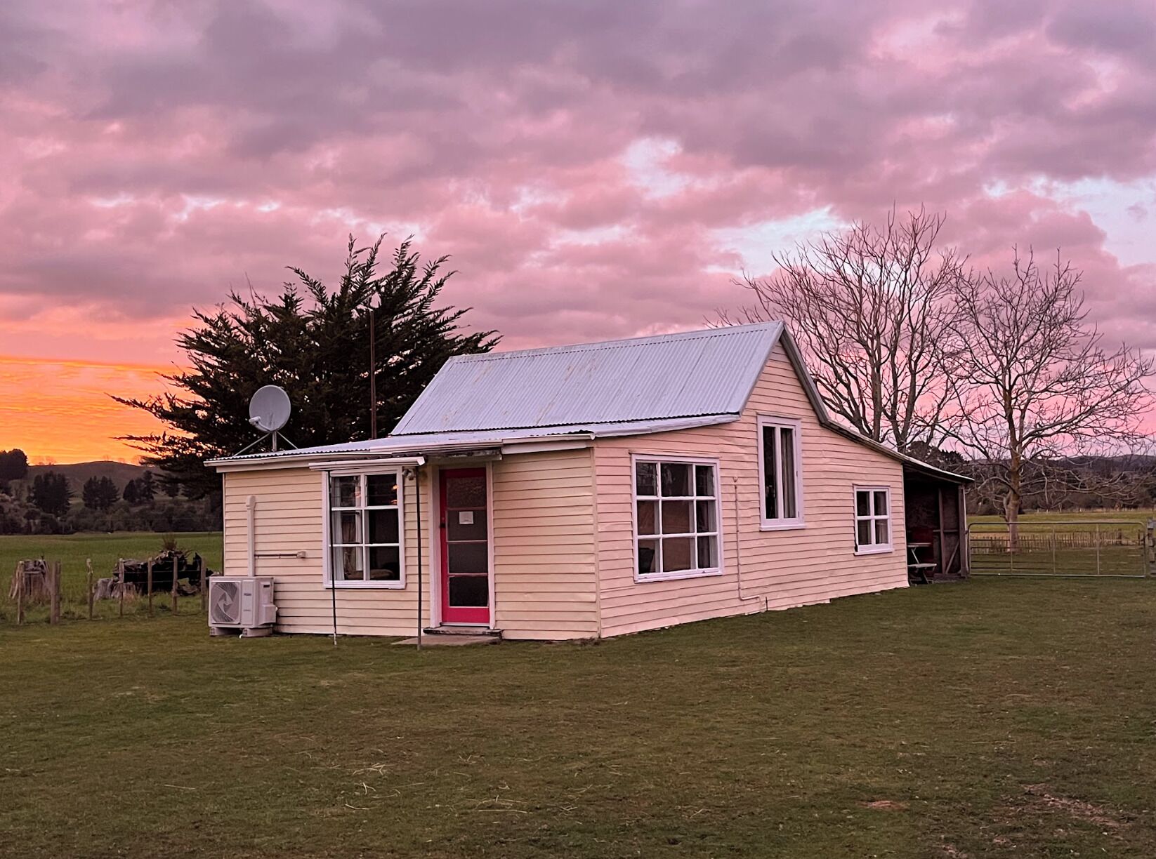 A single-story house with a red door, a satellite dish, and a metal roof.
