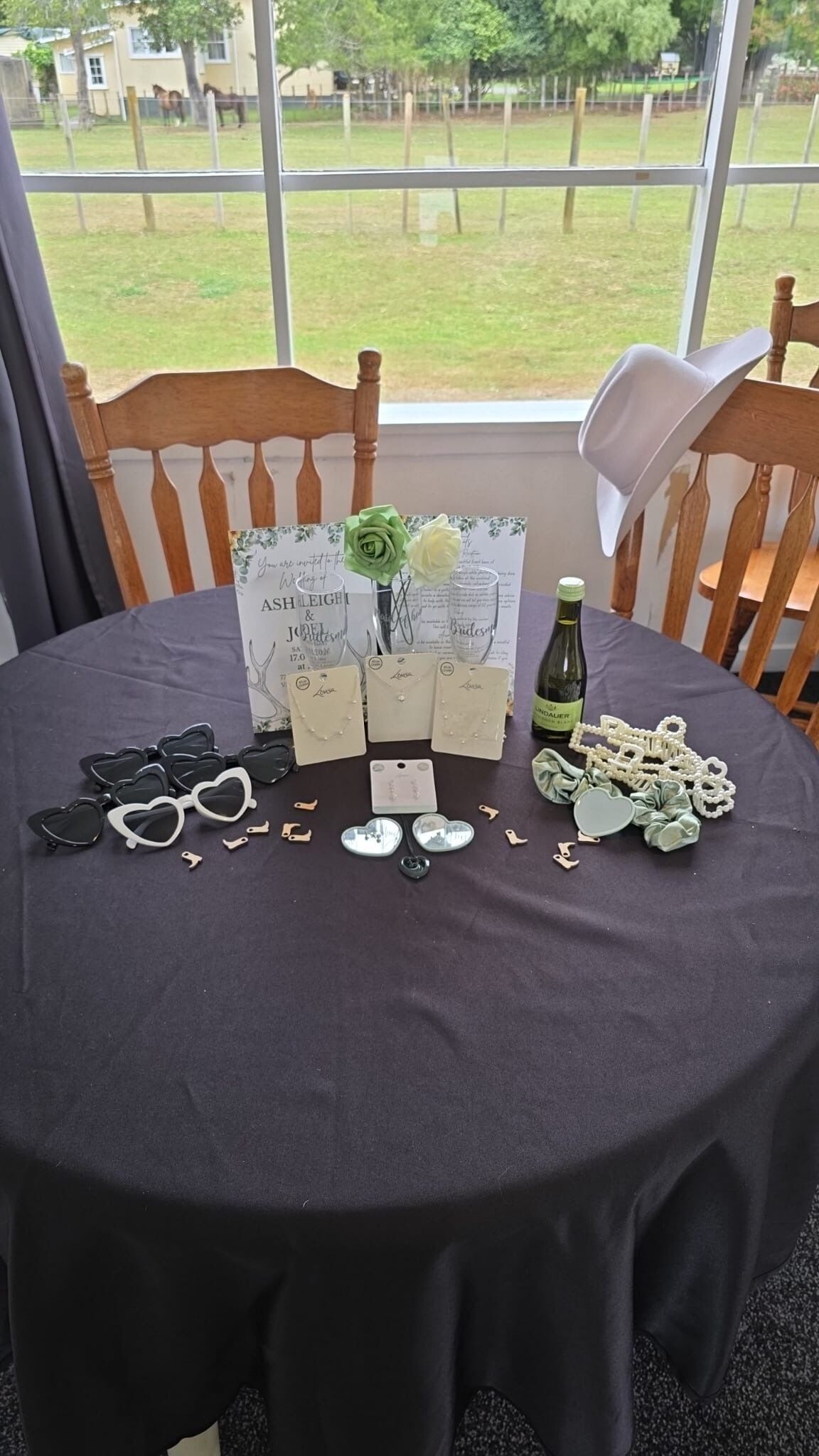 A table with a black tablecloth, a bottle of wine, and various items including heart-shaped sunglasses, jewelry, and a menu.