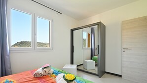 Um quarto com cama, uma pequena mesa de cabeceira, um espelho e um guarda-roupa.