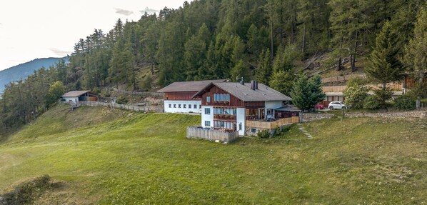 A hillside property with multiple wooden houses, a stone wall, and a grassy area. - Apartment 'Oberköbenhof Wohnung Berg' with Mountain View, Shared Terrace and Wi-Fi (Laces)