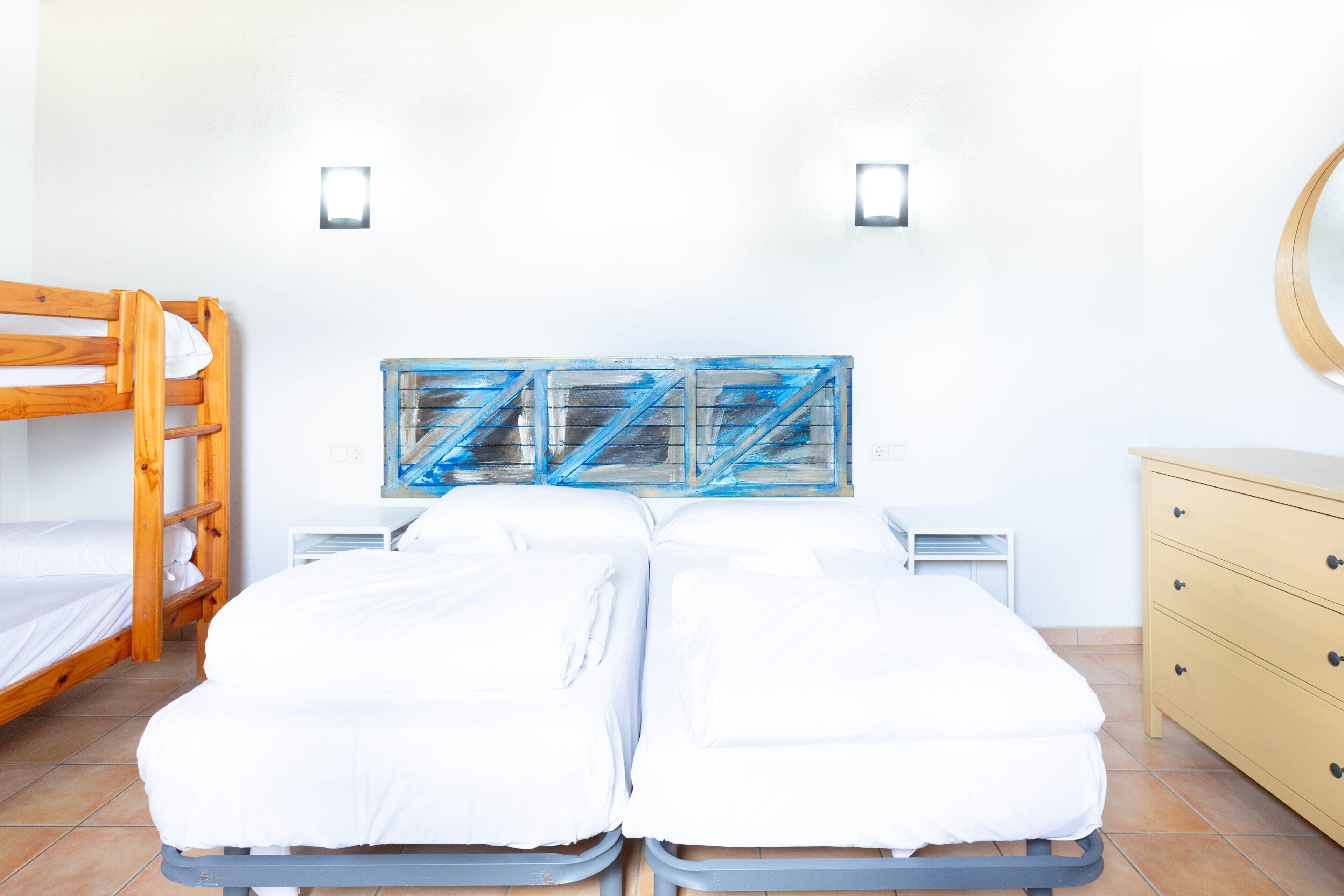 Een kamer met twee bedden, een stapelbed van hout, een dressoir en een spiegel aan de muur.