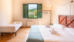 A bedroom with two beds, a view of greenery, a radiator, and a wooden chest of drawers. - Villa 'Mas Tortós' with Mountain View, Private Garden and Barbecue (Palafolls)