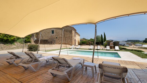 A covered outdoor area with lounge chairs, a pool, and a stone building. - Villa 'Mas Tortós' with Mountain View, Private Garden and Barbecue (Palafolls)