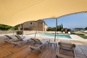 Un espacio al aire libre techado con sillones de descanso, una piscina y un edificio de piedra.