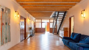 A spacious interior with a tiled floor, a blue sofa, a staircase, and wall-mounted lighting. - Villa 'Mas Tortós' with Mountain View, Private Garden and Barbecue (Palafolls)