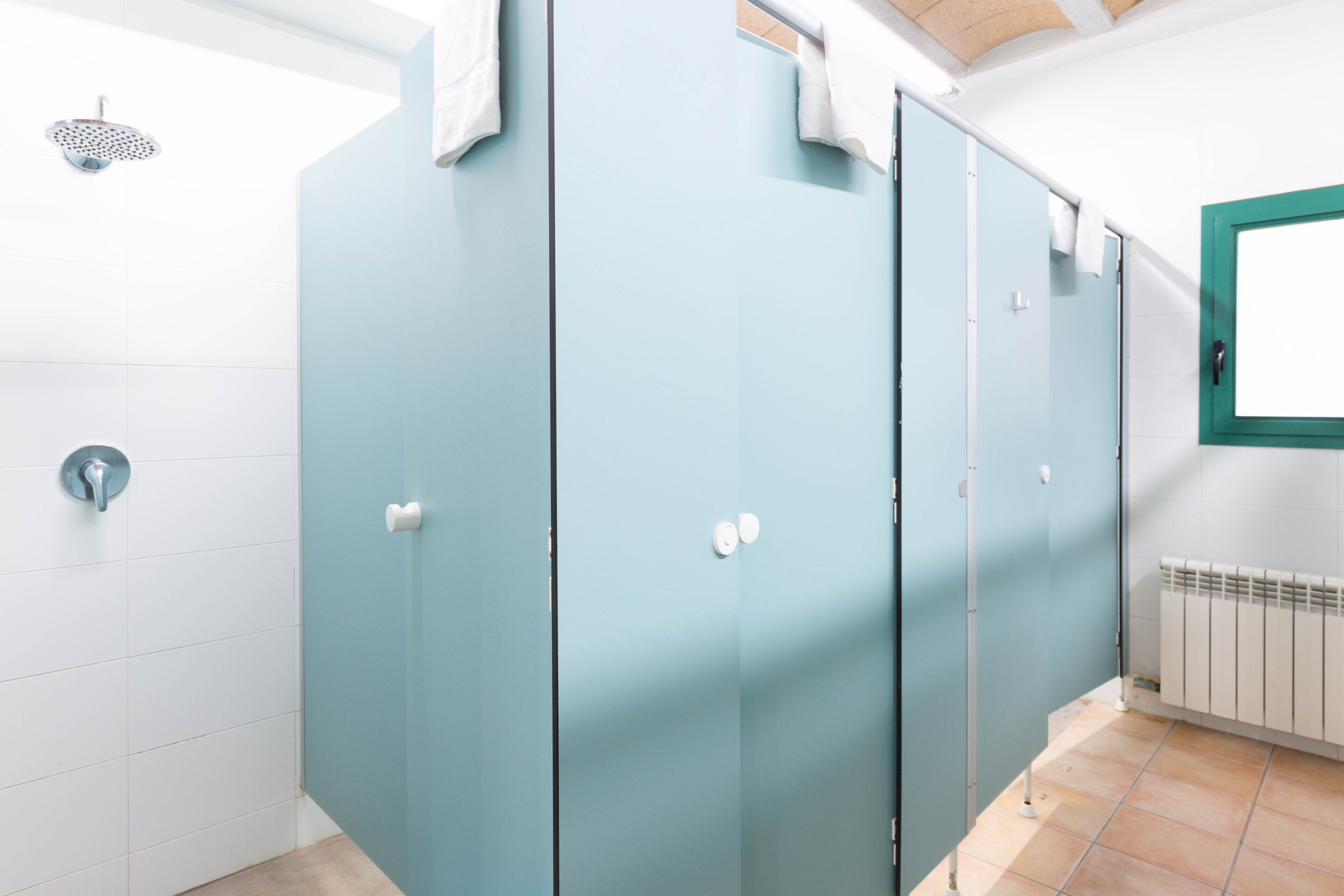 A restroom with blue stalls, a white radiator, and a window with a green frame.