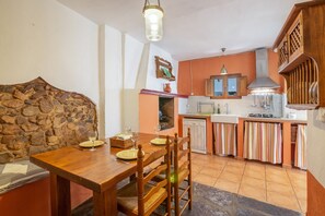 A dining area with a wooden table and chairs, a stone wall, and a kitchen with wooden cabinets and a tiled backsplash.