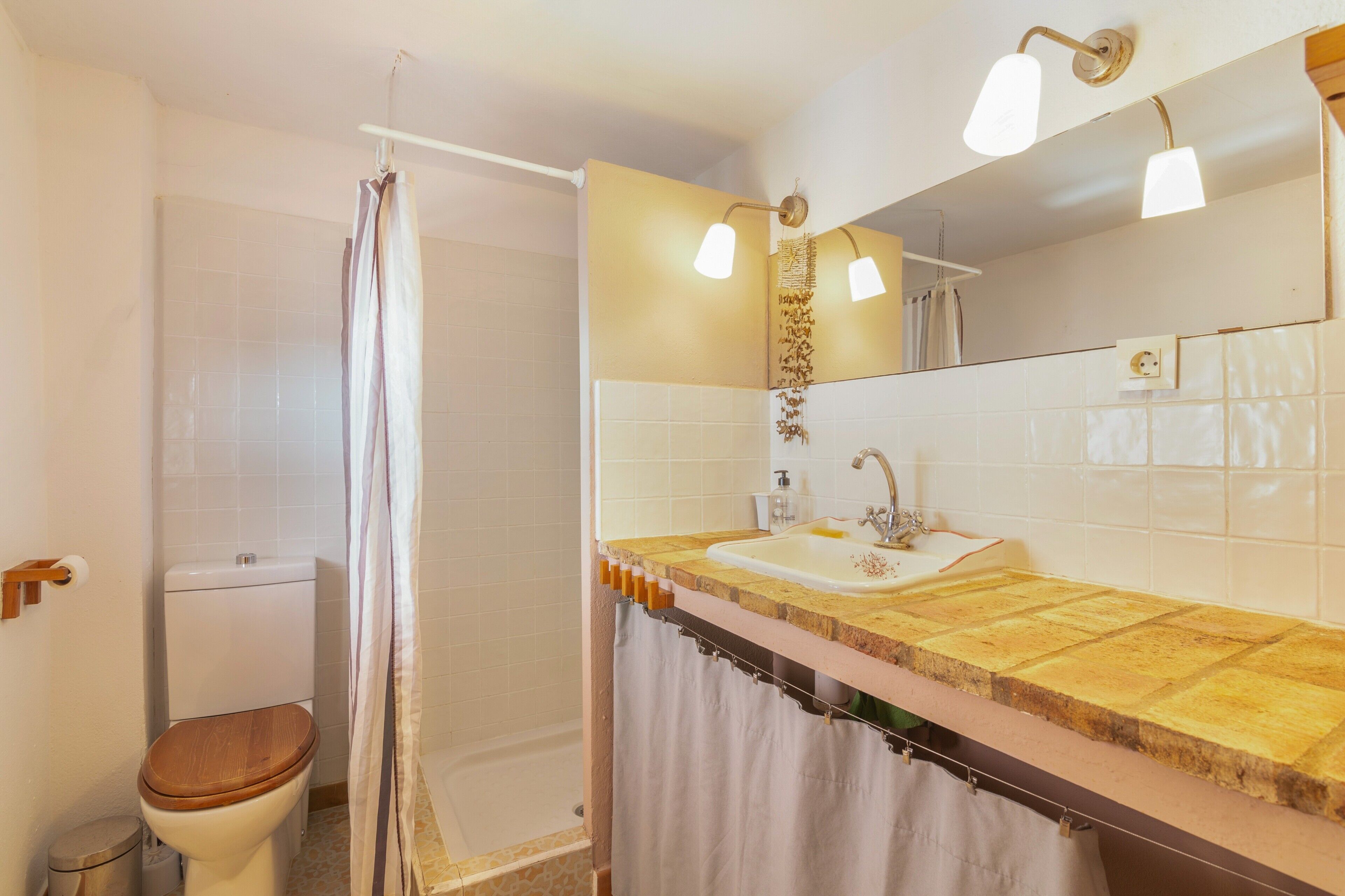 A bathroom with a toilet, shower, sink, and a mirror with lights.