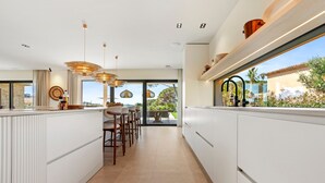 Une cuisine moderne avec des meubles blancs, un éclairage suspendu et une vue sur l’extérieur.