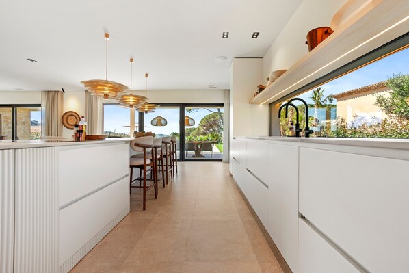 A modern kitchen with white cabinetry, pendant lighting, and a view of the outdoors.