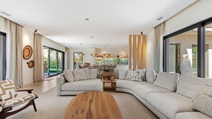 Un salon moderne avec un grand canapé en forme de L, une table basse en bois et un coin repas à l’arrière-plan.