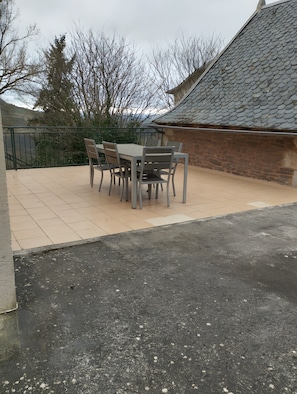An outdoor patio with a table and chairs, a stone wall, and a tiled floor.