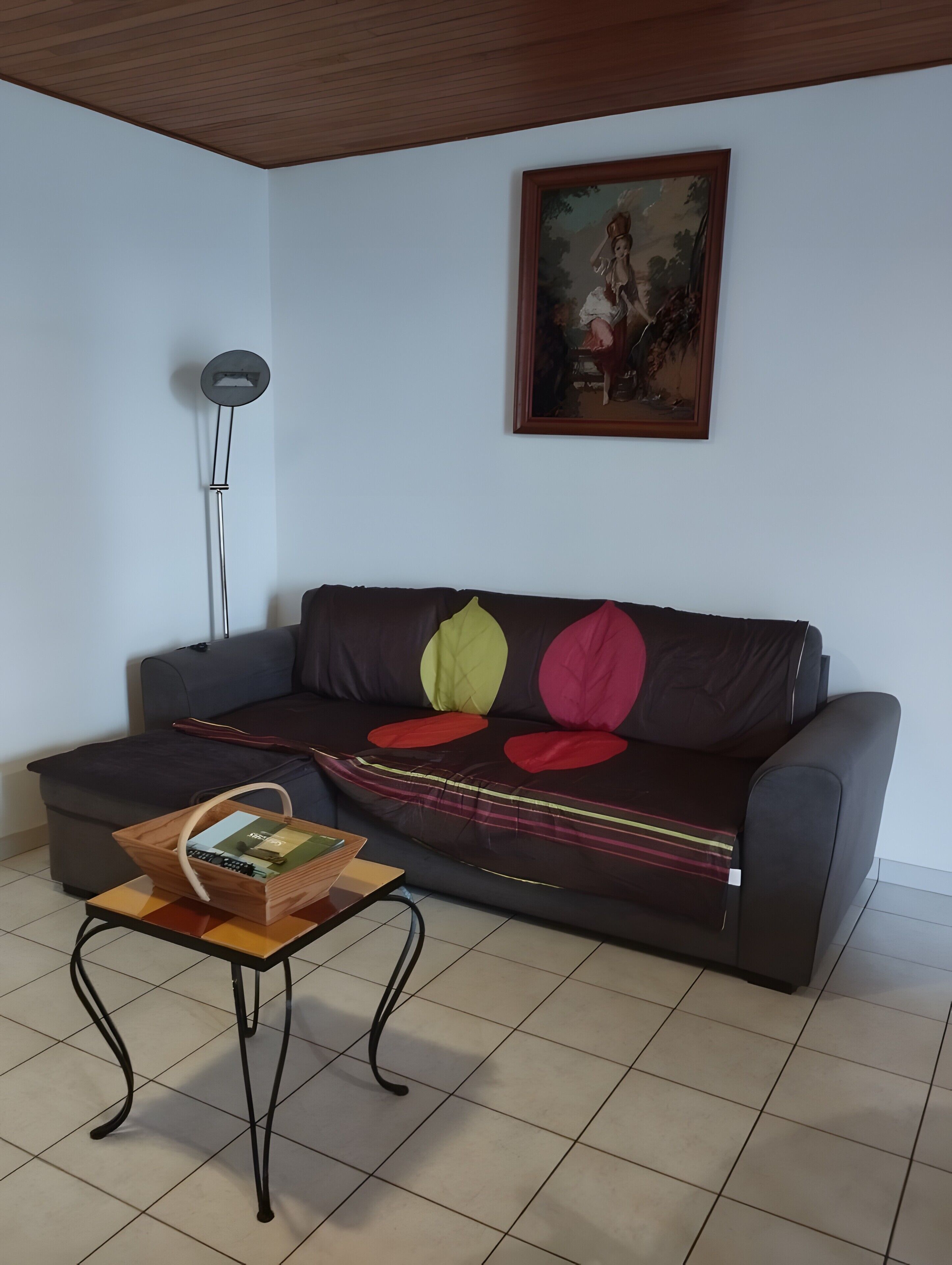 A living room with a sofa, a small table with a basket, a floor lamp, and a painting on the wall.