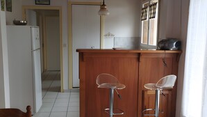 Una cocina con encimera de madera, dos taburetes de bar, un refrigerador y una mesa de comedor con mantel estampado.