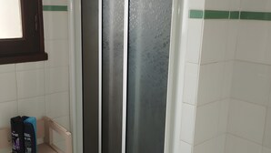 Un baño con cabina de ducha, un estante con artículos de aseo y una ventana con vistas al exterior.