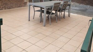 Un patio con una mesa y sillas, una parrilla de barbacoa y un edificio de piedra con techo de tejas.