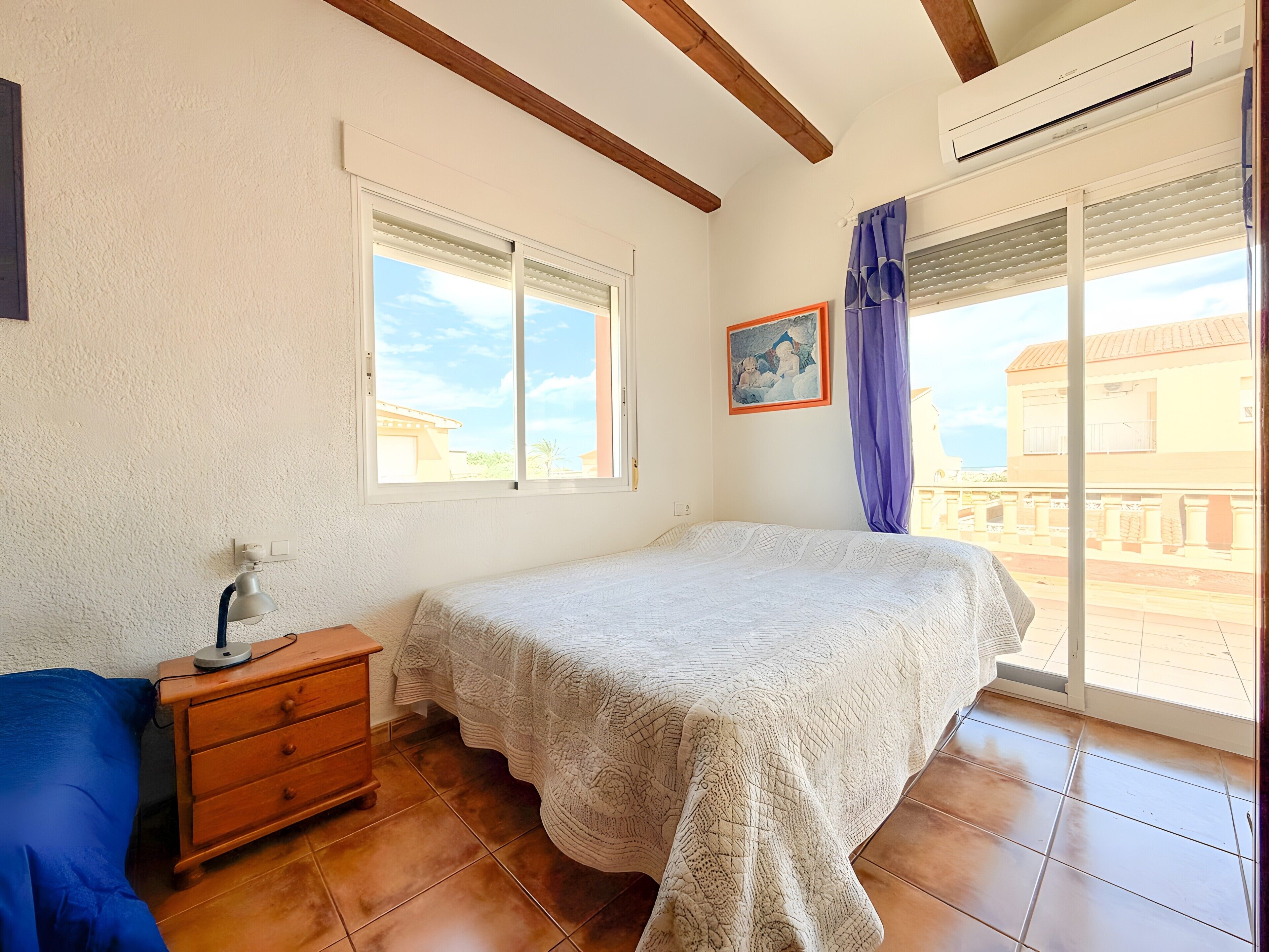 Une chambre à coucher avec un lit, une commode, une lampe, un tableau et une fenêtre donnant sur un beau paysage.