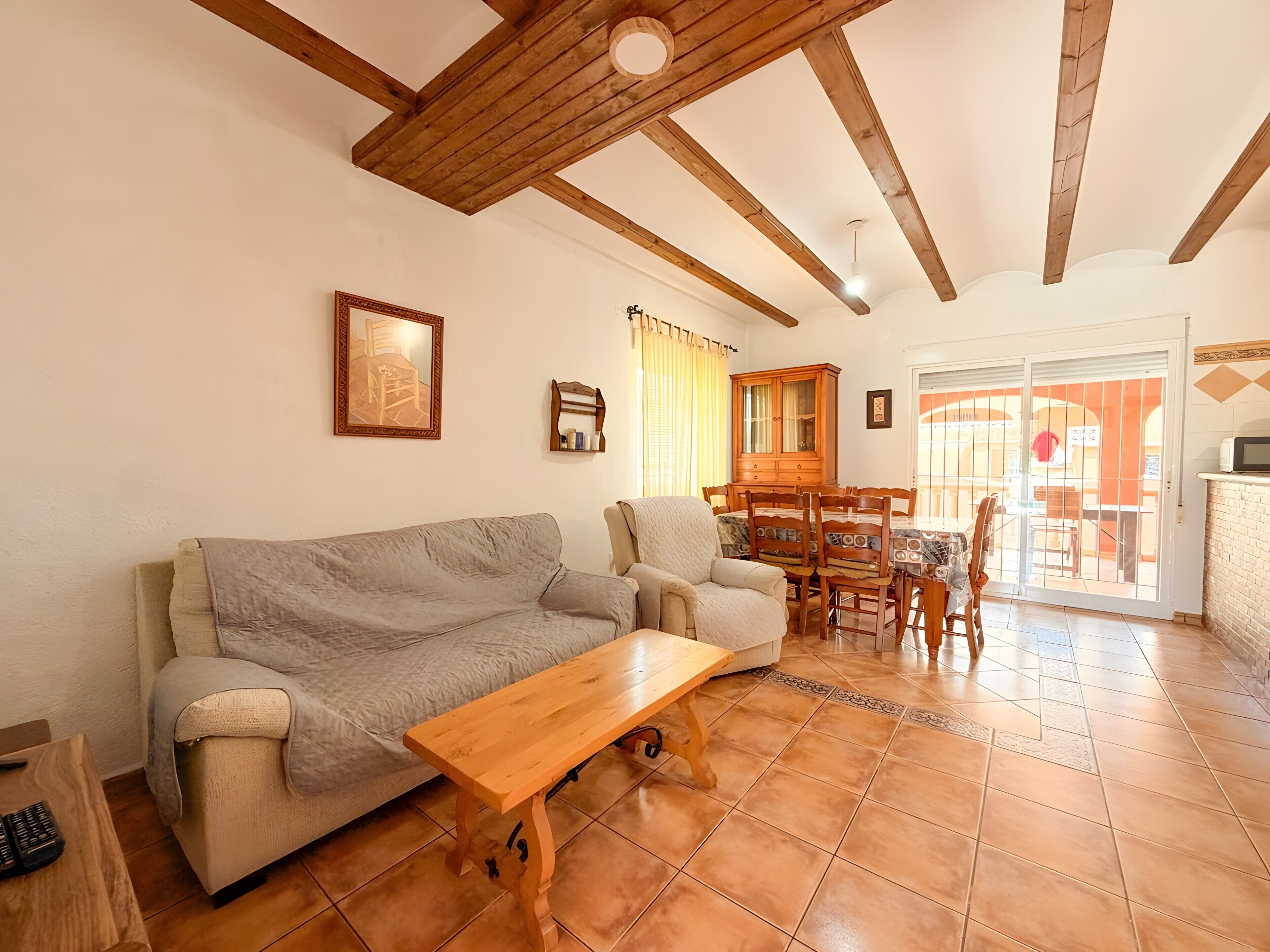 A living room with a sofa, armchair, wooden coffee table, and a dining area with chairs and a cabinet.