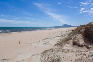 Une plage de sable bordée d’une clôture, avec l’océan et une montagne qui se dessine à l’horizon.