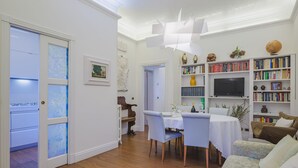 A modern living room with a dining area, wooden flooring, white walls, and a bookshelf filled with books and decorative items. - Onda Marina by Interhome (Bocca di Magra)
