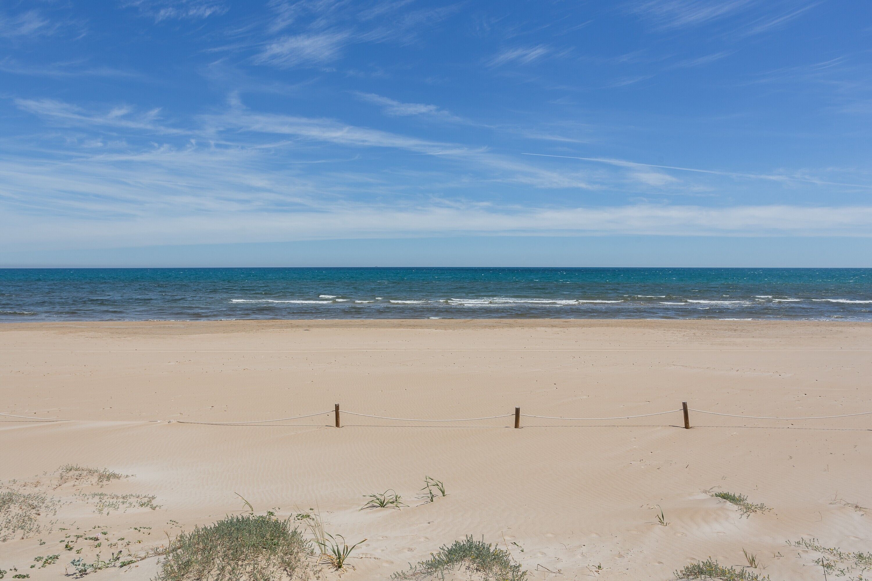 Ein Strand mit einem Zaun, blauem Himmel und dem Meer.