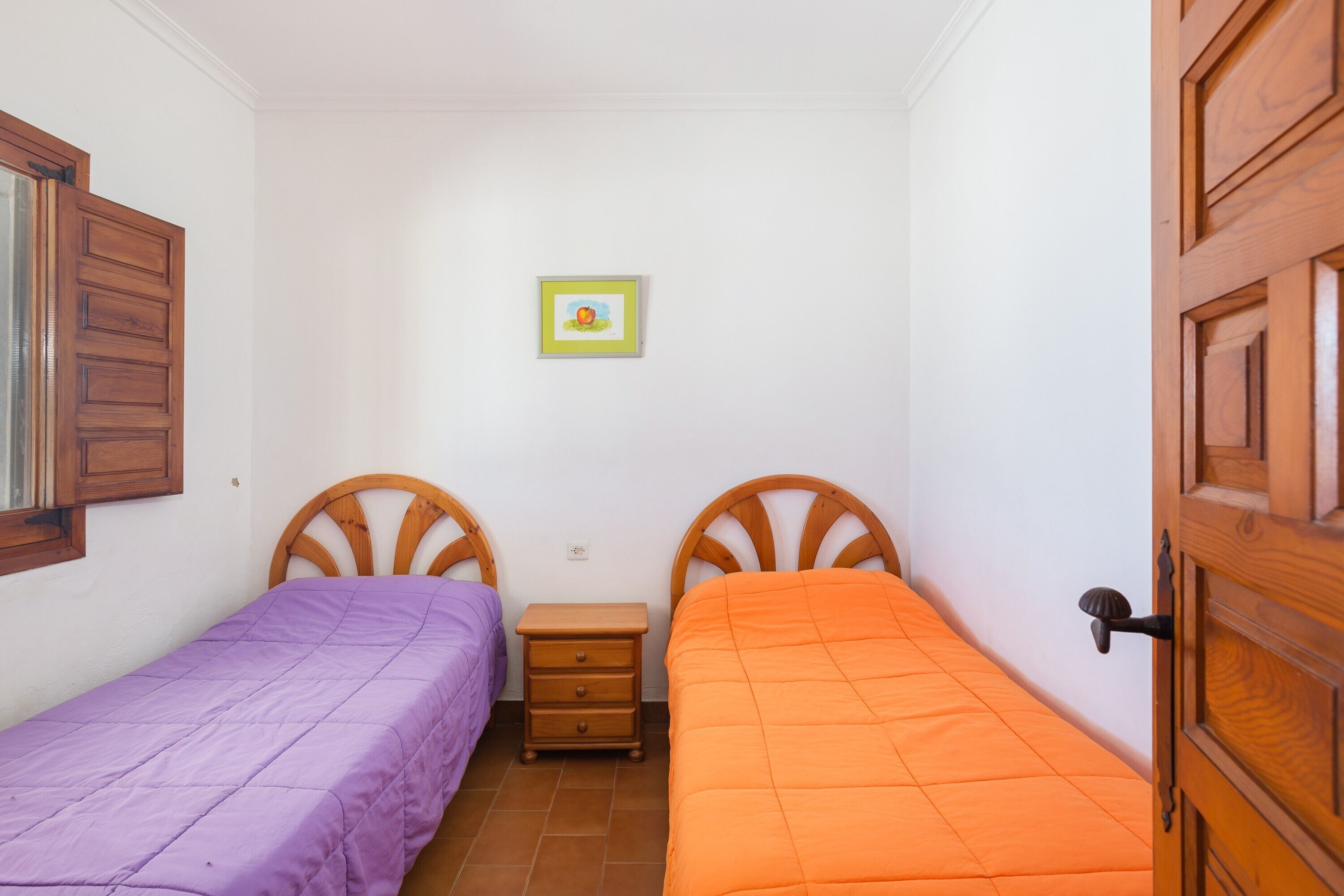 A small room with two beds, a wooden nightstand, a wall-mounted picture, and a wooden door.
