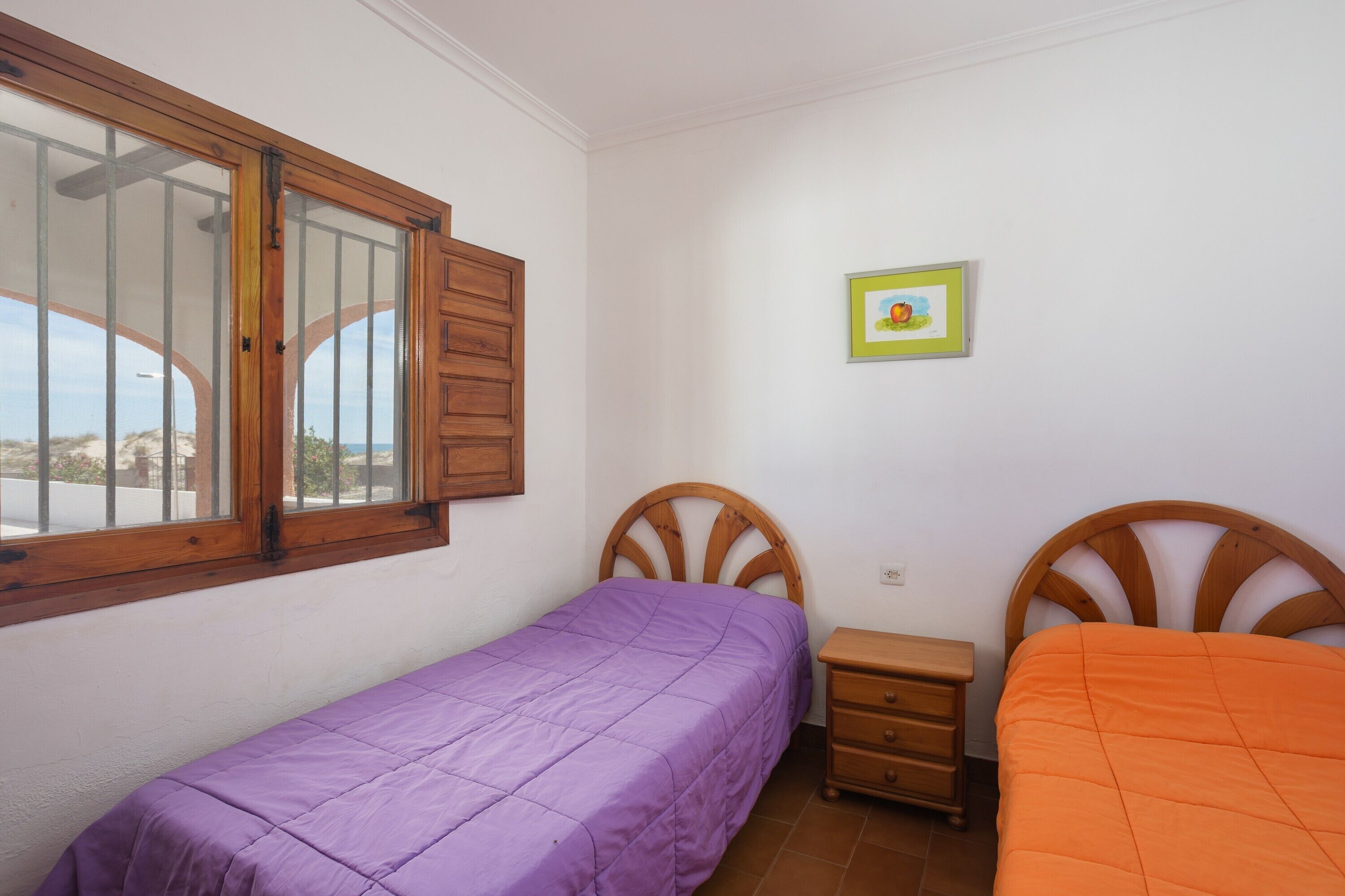 A bedroom with two beds, a window, a dresser, and a framed picture on the wall.