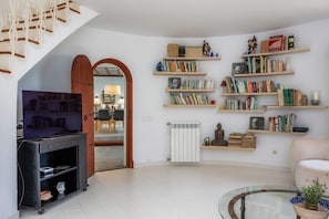 Een woonkamer met een televisie, boekenkasten, een radiator en een glazen salontafel.