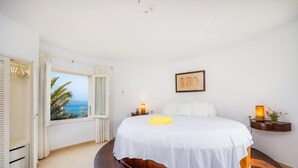 Une chambre à coucher comprenant un lit, une table de chevet, une commode, une fenêtre donnant sur un paysage agréable et une porte.