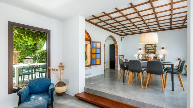Un intérieur moderne avec un fauteuil bleu, un coin repas avec des chaises et un escalier menant à un deuxième niveau.