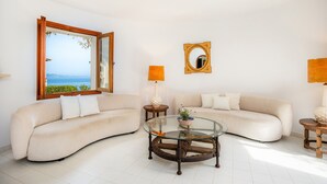 Un salon avec deux canapés, une table basse en verre, un miroir et une vue sur la mer.