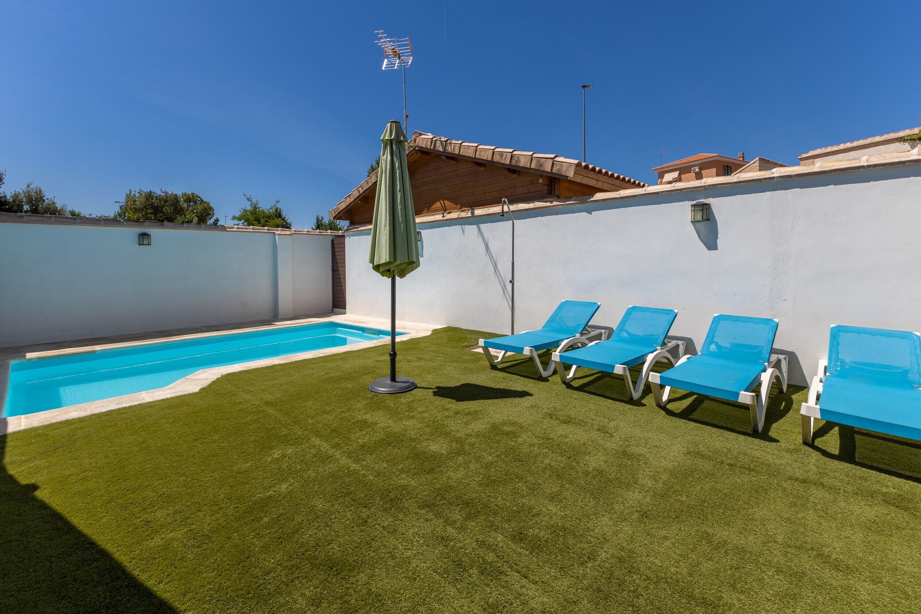 Une piscine bordée de gazon synthétique, un parasol et des chaises longues bleues.