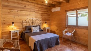 Ein Schlafzimmer einer Holzhütte mit einem Bett, zwei Nachttischen, einem Sessel und einem Fenster.