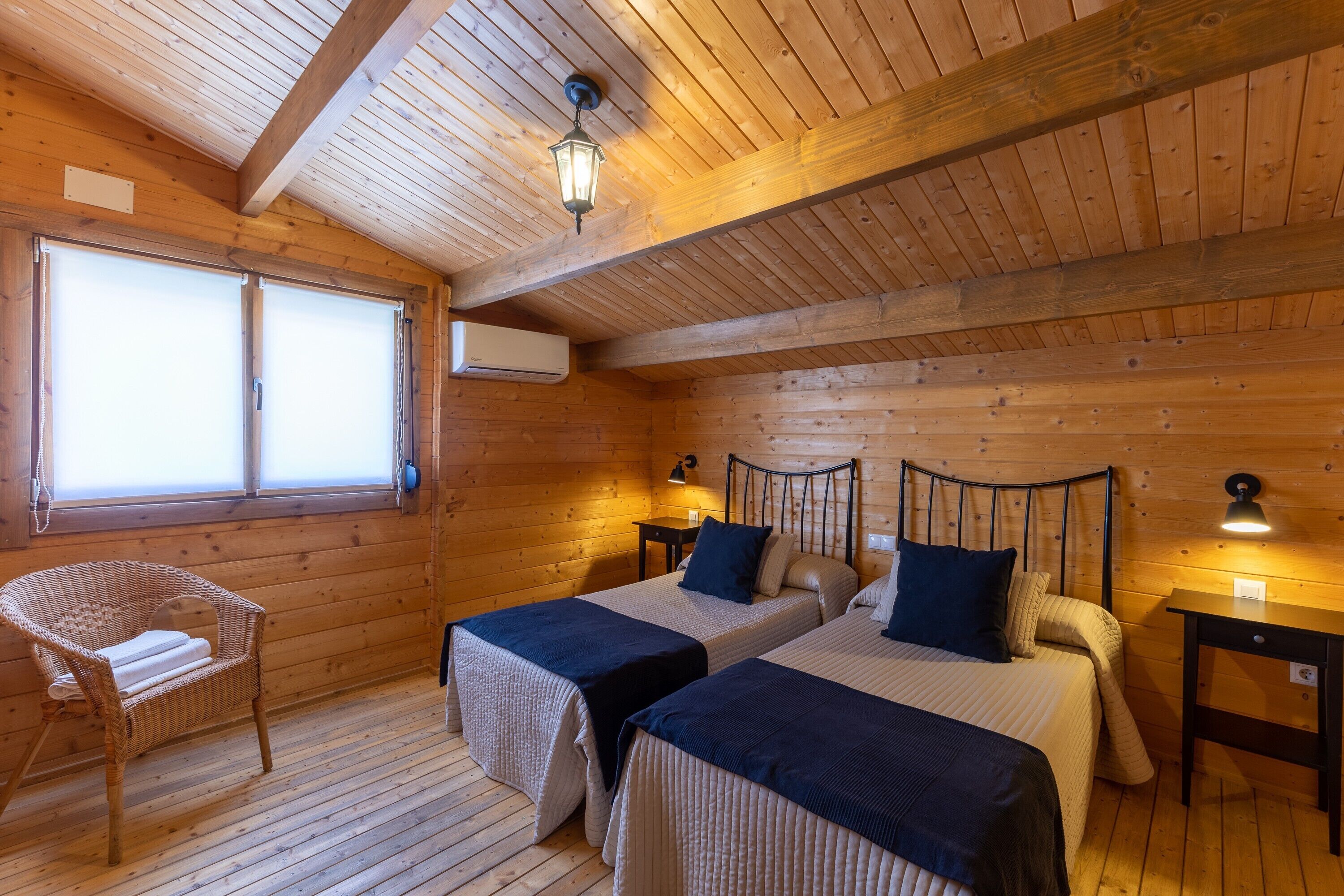 Una habitación de cabaña de madera con dos camas, una silla y una ventana.