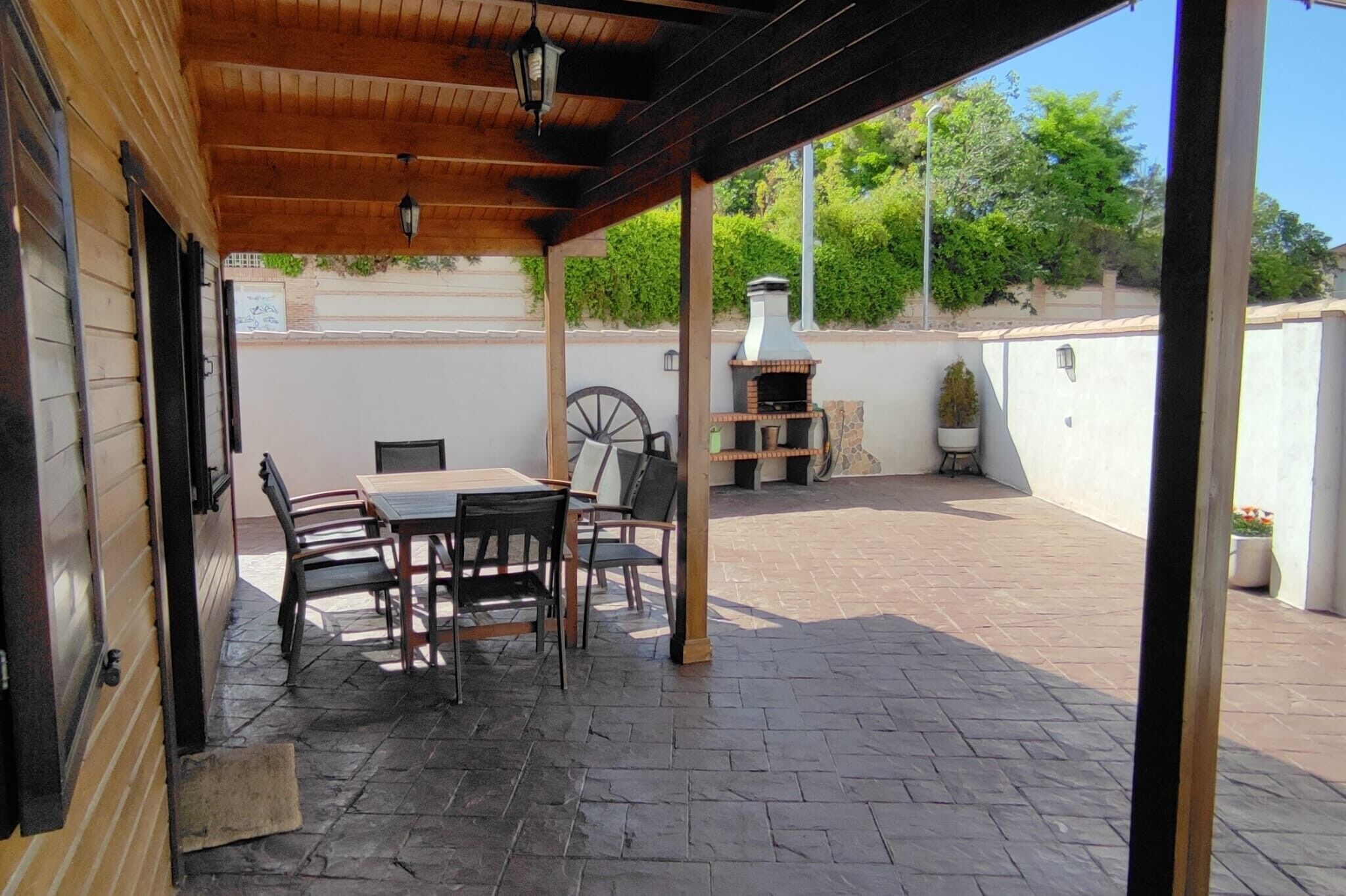 An outdoor patio with a table and chairs, a wooden pergola, a brick floor, and a brick oven.
