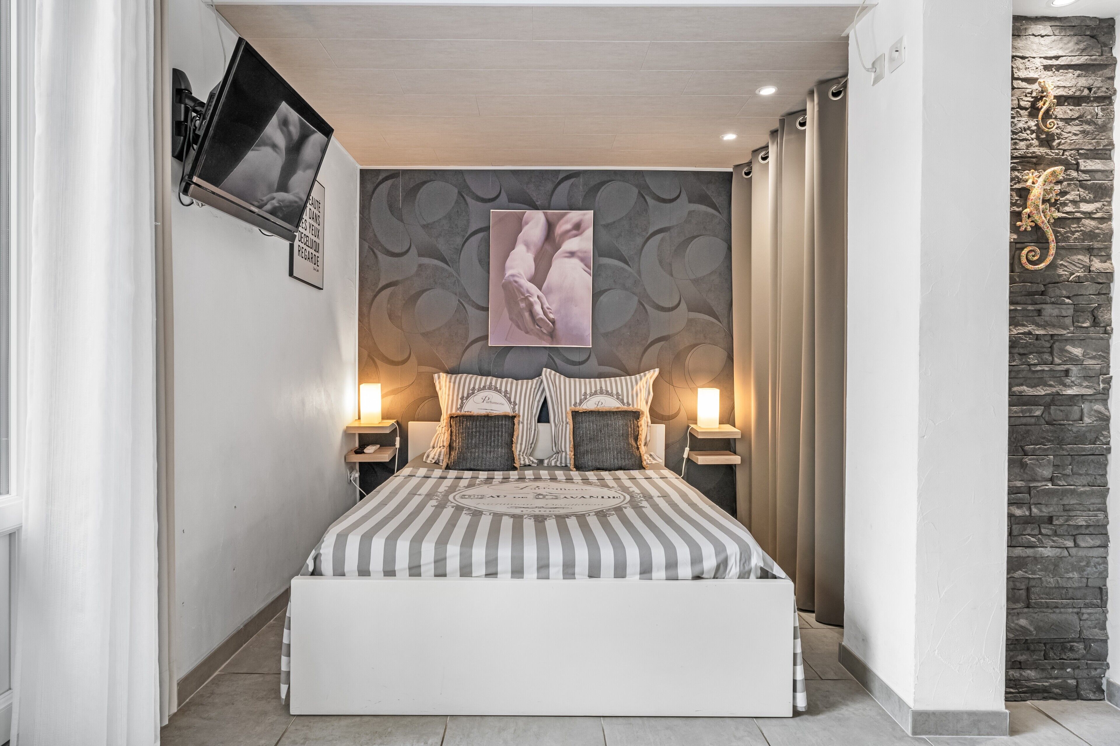 Une chambre avec un lit, un téléviseur fixé au mur, une œuvre d’art accrochée au mur et un mur d’accent en pierre.