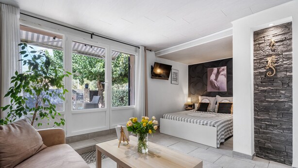 Habitació moderna amb un sofà, una taula petita amb un ram de flors, un llit amb edredó rayat i una paret d'accent de pedra.