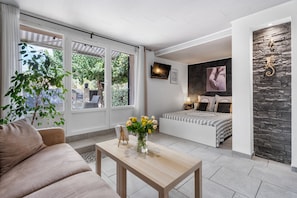 Una habitación moderna con sofá, una mesita con un jarrón de flores, cama con colcha a rayas y una pared de piedra decorativa.