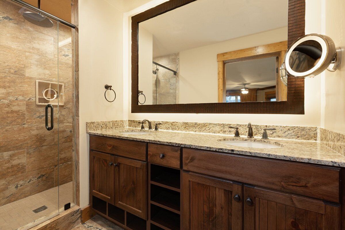 A bathroom with a glass shower enclosure, a large mirror, and wooden cabinets.