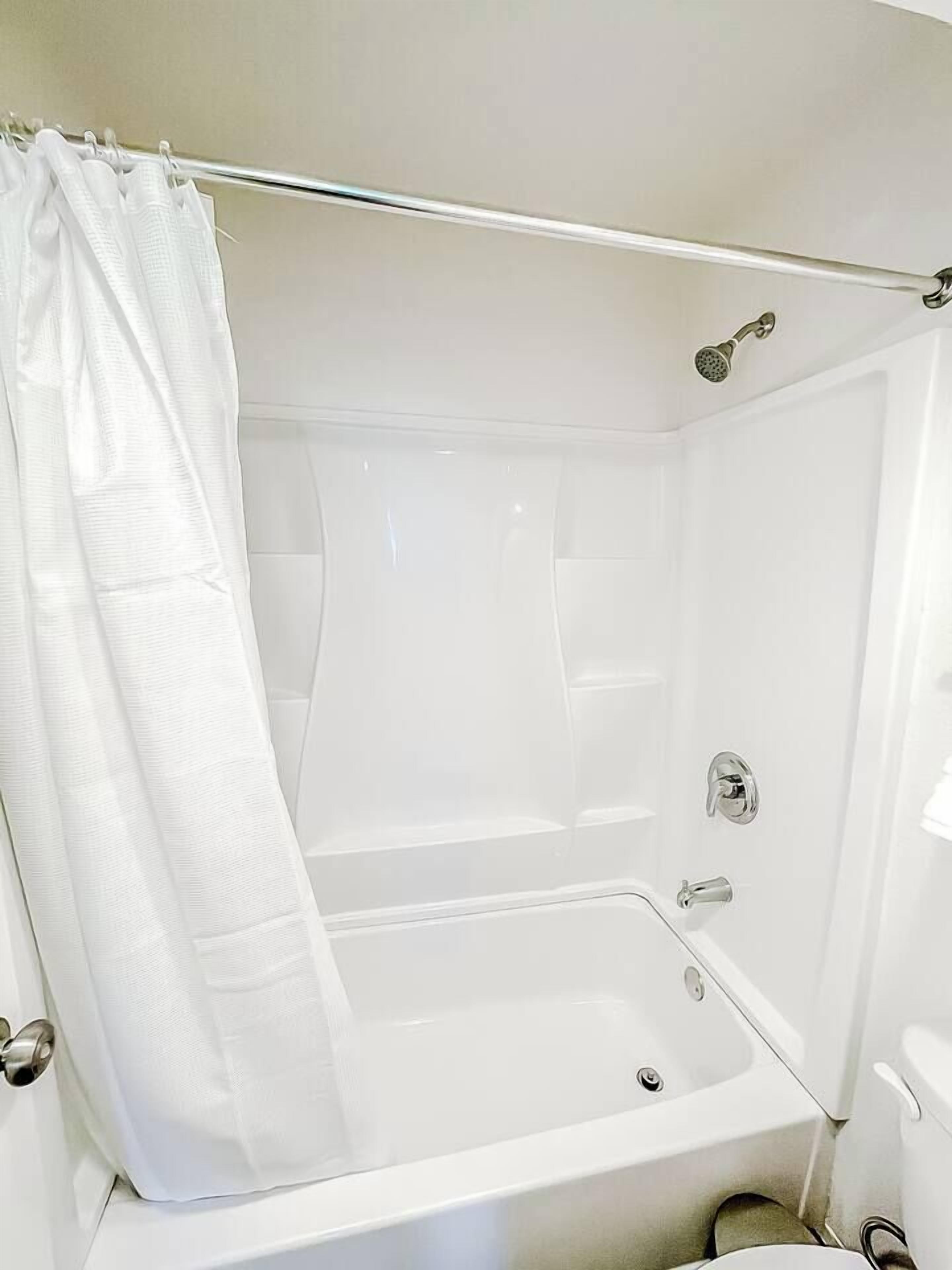 A white bathtub with a shower curtain, a handheld showerhead, and a faucet.
