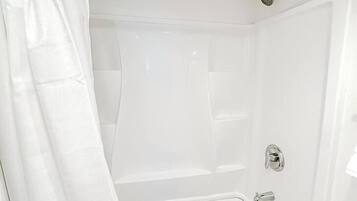 A white bathtub with a shower curtain, a handheld showerhead, and a faucet.