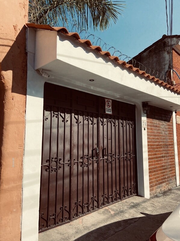 Un edificio residencial con entrada protegida por una reja, un cartel de prohibido estacionar y un número de domicilio visible.