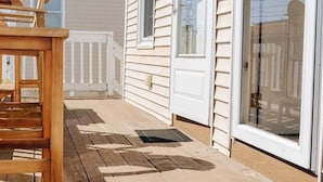 A wooden deck with a chair, a white house with a sliding glass door, and a white picket fence.