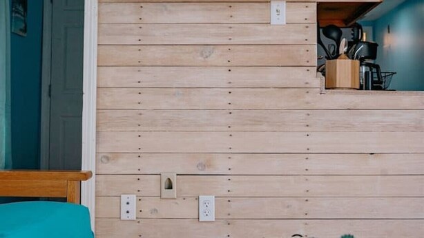 A room with a wooden wall, a bed, a table, and a painting of a pier.